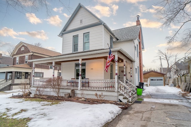 view of front of property with aphalt driveway, an outbuilding, a chimney, a porch, and a garage