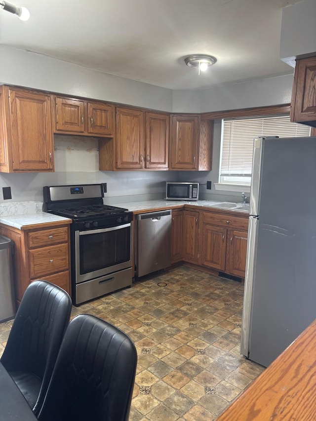 kitchen with a sink, stainless steel appliances, light countertops, and brown cabinets