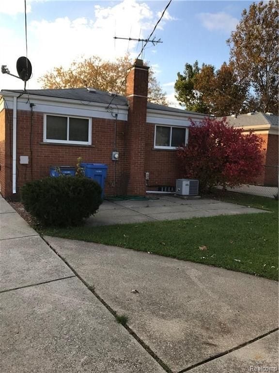 back of property featuring brick siding, a yard, a chimney, a patio, and fence