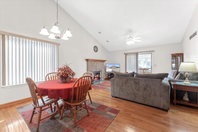 dining space featuring high vaulted ceiling, hardwood / wood-style flooring, ceiling fan with notable chandelier, a fireplace, and visible vents