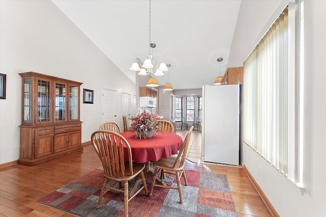 dining area featuring baseboards, high vaulted ceiling, light wood-type flooring, and an inviting chandelier