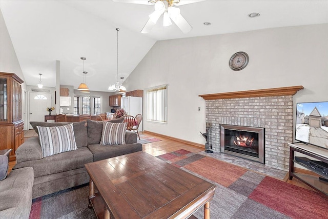 living room featuring baseboards, a ceiling fan, wood finished floors, a brick fireplace, and high vaulted ceiling