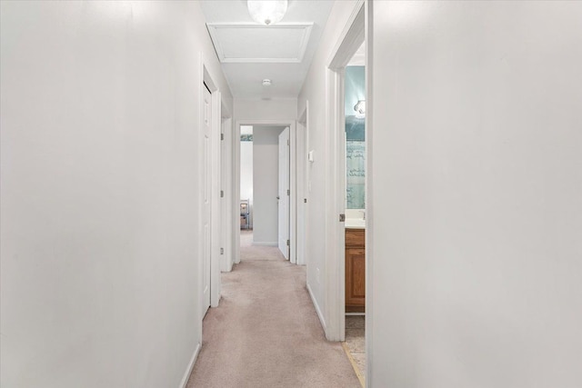 corridor featuring light carpet, attic access, and baseboards