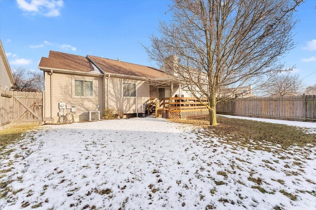 snow covered house featuring central AC, a chimney, a wooden deck, and fence