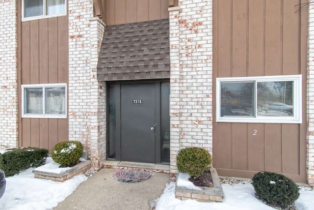 snow covered property entrance with roof with shingles