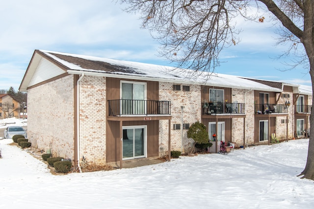 snow covered rear of property featuring brick siding and a balcony