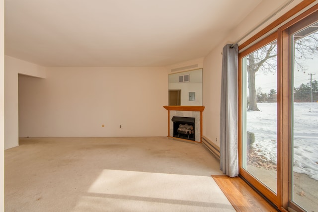 unfurnished living room featuring baseboard heating, light colored carpet, and a tile fireplace