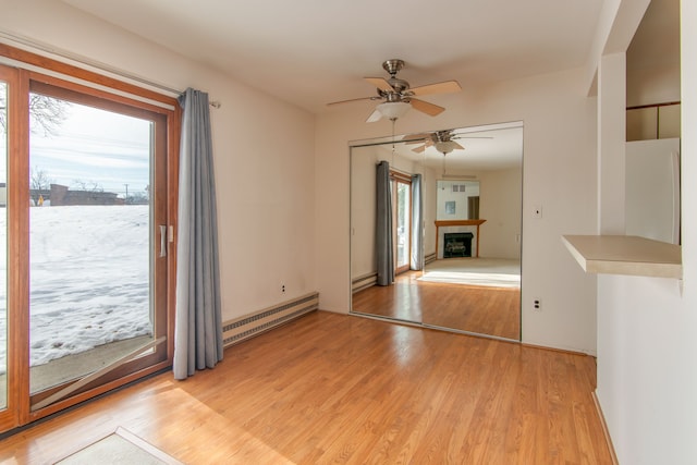 spare room featuring a baseboard radiator, ceiling fan, light wood-style flooring, and a tile fireplace