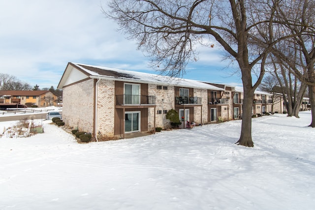 snow covered rear of property featuring brick siding