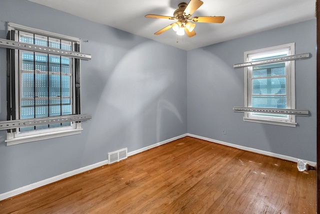 empty room with ceiling fan, hardwood / wood-style floors, visible vents, and baseboards