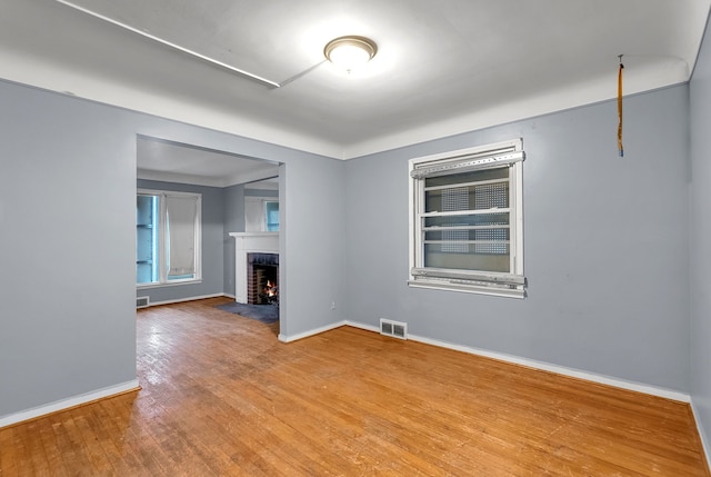 unfurnished living room featuring a fireplace with flush hearth, visible vents, baseboards, and hardwood / wood-style flooring