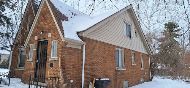 view of snowy exterior with cooling unit and brick siding