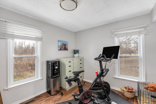 workout area featuring visible vents, a textured ceiling, baseboards, and wood finished floors