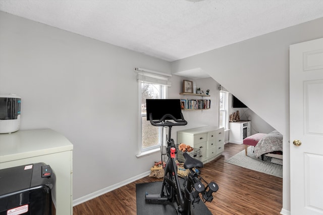 workout room featuring a textured ceiling, baseboards, and wood finished floors