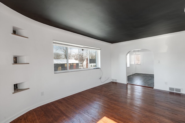 unfurnished room featuring arched walkways, dark wood-style floors, and visible vents