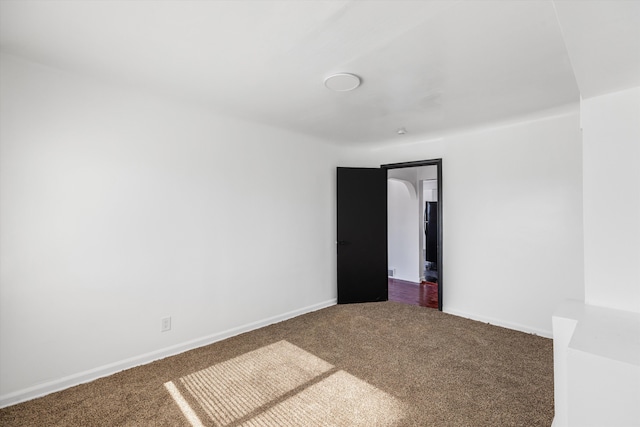 empty room with dark colored carpet and baseboards