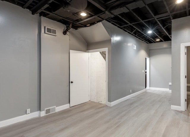 below grade area with light wood-style flooring, visible vents, and baseboards