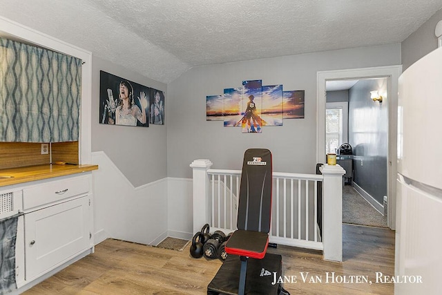 interior space featuring light wood finished floors, vaulted ceiling, a textured ceiling, and an upstairs landing