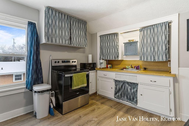 kitchen featuring black microwave, electric stove, light wood finished floors, and white cabinetry