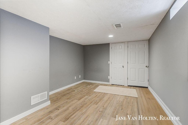 empty room featuring light wood-style floors, baseboards, visible vents, and a textured ceiling