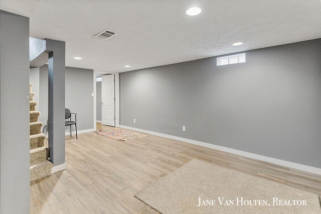 basement with visible vents, a textured ceiling, light wood-type flooring, baseboards, and stairs