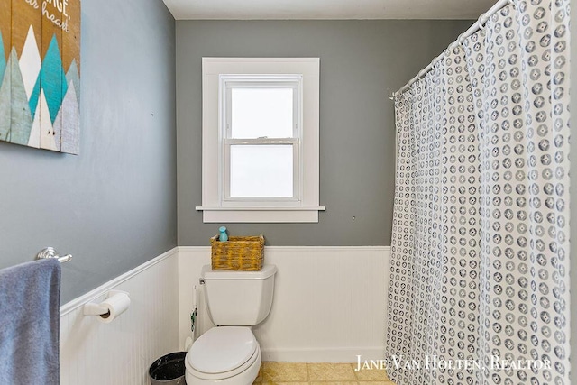 full bathroom featuring curtained shower, a wainscoted wall, toilet, and tile patterned floors