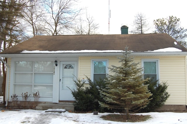 snow covered property featuring a shingled roof and a chimney