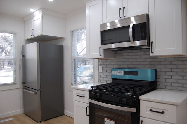 kitchen featuring appliances with stainless steel finishes, white cabinetry, ornamental molding, and light stone counters