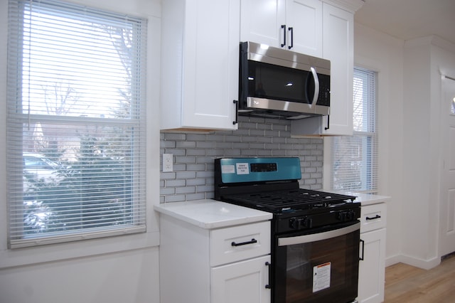 kitchen with white cabinets, stainless steel microwave, black gas stove, and decorative backsplash