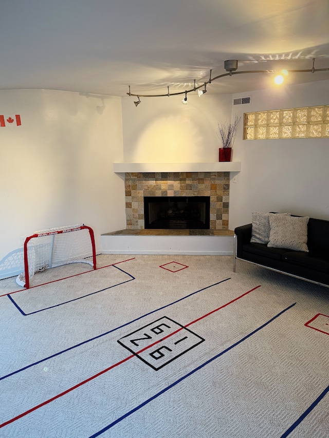 unfurnished living room featuring carpet floors, a fireplace with raised hearth, visible vents, and track lighting