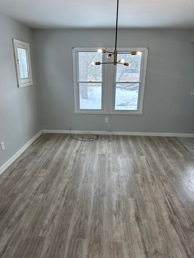 unfurnished dining area featuring an inviting chandelier, plenty of natural light, baseboards, and wood finished floors