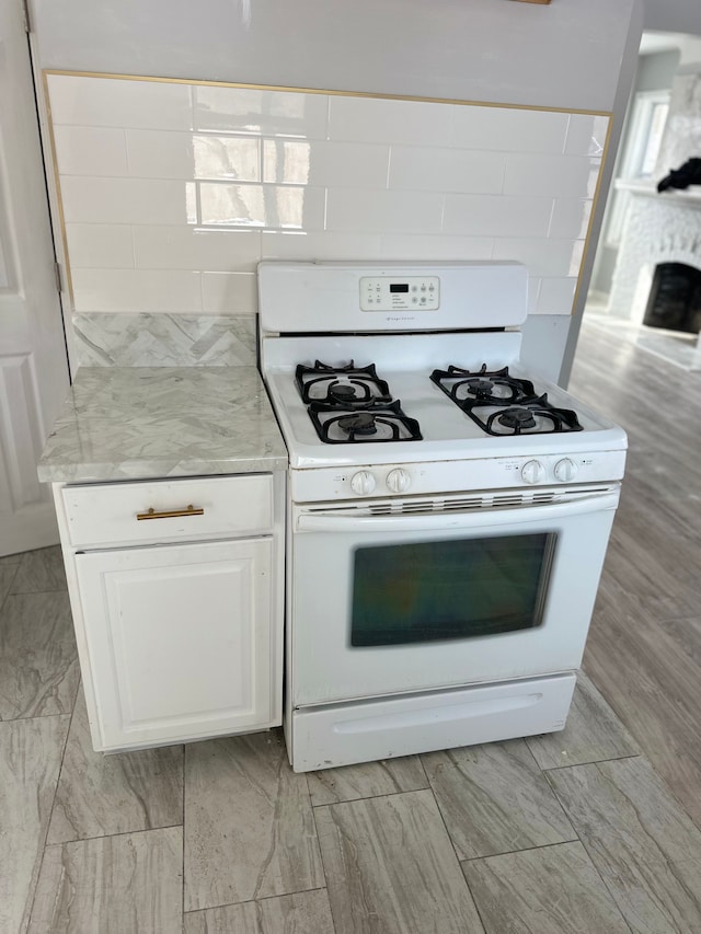 kitchen with a fireplace, white cabinets, backsplash, and white gas stove