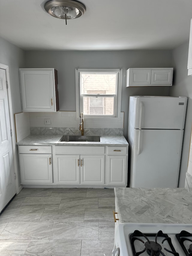 kitchen with freestanding refrigerator, white cabinetry, a sink, and gas stove