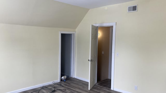 unfurnished bedroom with lofted ceiling, visible vents, dark wood finished floors, and baseboards