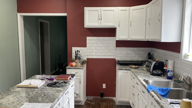 kitchen with tasteful backsplash, a sink, white cabinetry, and light stone countertops