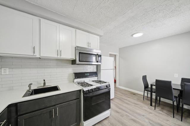 kitchen featuring light wood finished floors, light countertops, white cabinets, a sink, and white appliances