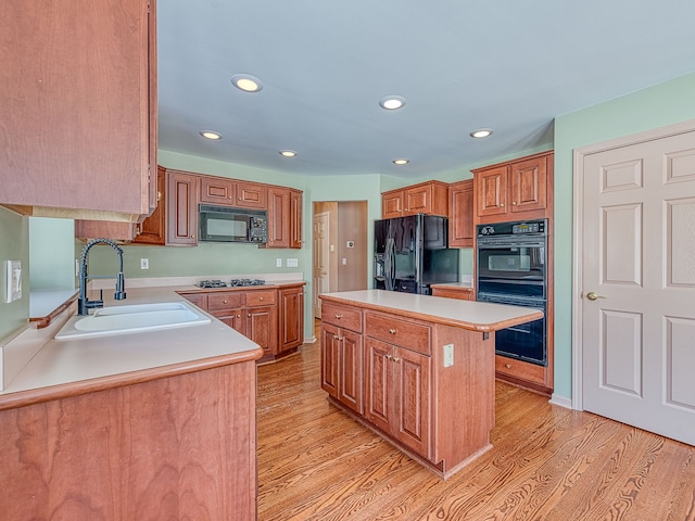 kitchen featuring light countertops, a sink, a kitchen island, light wood-type flooring, and black appliances