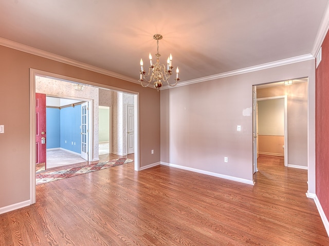 spare room with a notable chandelier, baseboards, ornamental molding, and wood finished floors