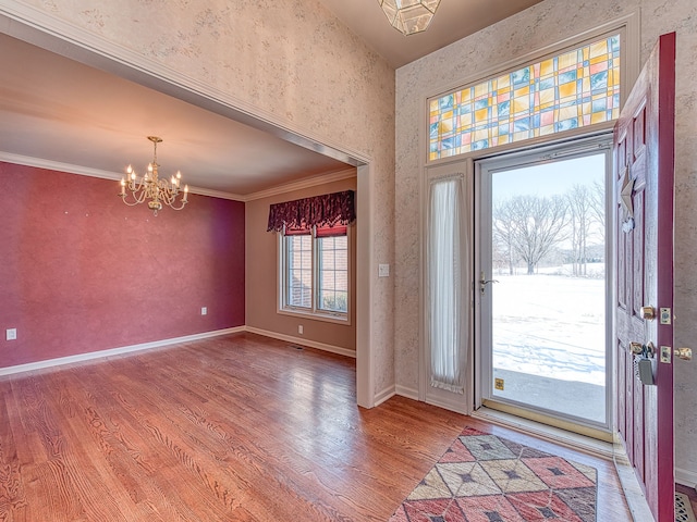 foyer entrance with wallpapered walls, baseboards, ornamental molding, wood finished floors, and an inviting chandelier