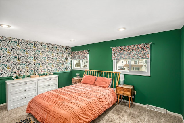 carpeted bedroom featuring wallpapered walls, baseboards, visible vents, and a wainscoted wall