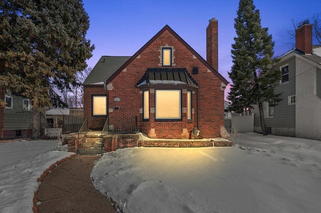 tudor home with brick siding, a chimney, a standing seam roof, metal roof, and fence