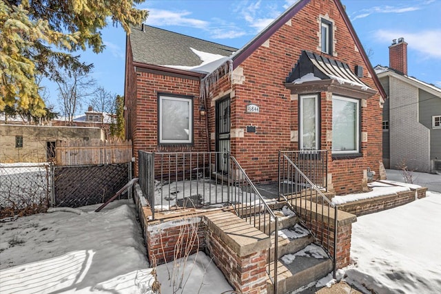 view of front of house featuring brick siding, a shingled roof, and fence