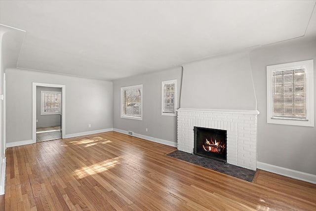 unfurnished living room with a brick fireplace, wood finished floors, visible vents, and baseboards