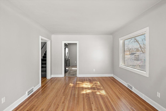 spare room with light wood-type flooring, visible vents, baseboards, and stairs