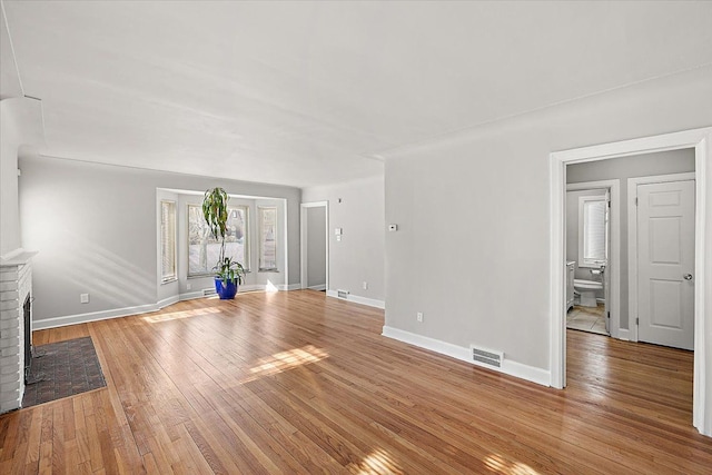 unfurnished living room with a brick fireplace, wood finished floors, visible vents, and baseboards