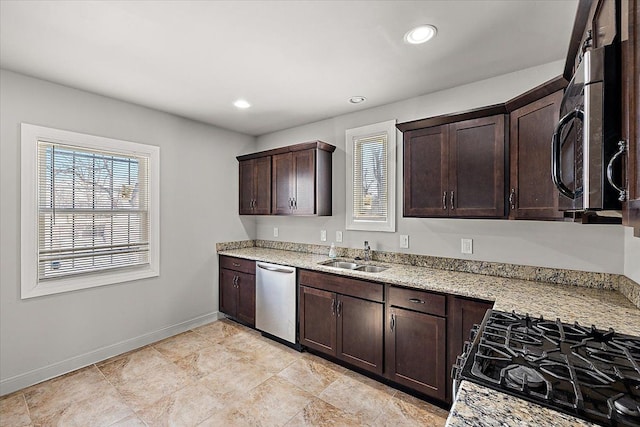 kitchen featuring stainless steel appliances, a sink, dark brown cabinets, and light stone countertops