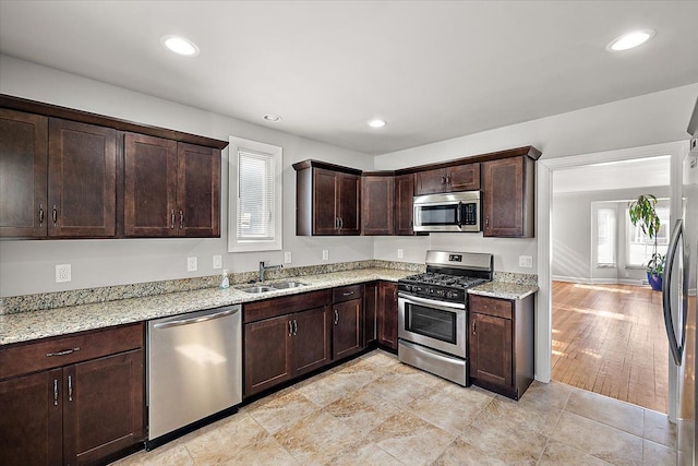 kitchen featuring light stone counters, stainless steel appliances, recessed lighting, a sink, and dark brown cabinets