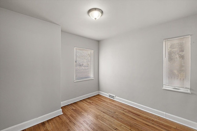 empty room featuring wood finished floors, visible vents, and baseboards