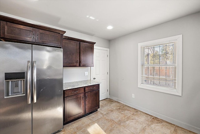 kitchen featuring dark brown cabinets, light stone counters, stainless steel fridge, and baseboards