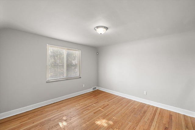 spare room featuring lofted ceiling, light wood finished floors, visible vents, and baseboards